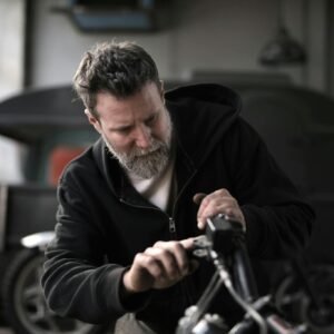 Concentrated male biker in casual wear fixing motorcycle part while working in garage