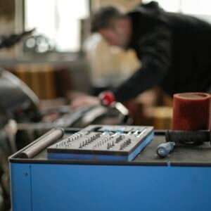 Plastic toolbox with small metal details placed on metal workbench in spacious garage while faceless adult  male mechanic repairing motorbike